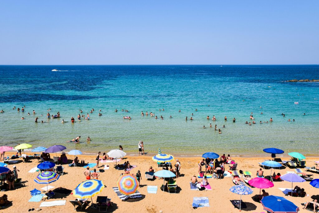 Crowded beach day with colorful umbrellas and swimmers in Apulia, Italy.