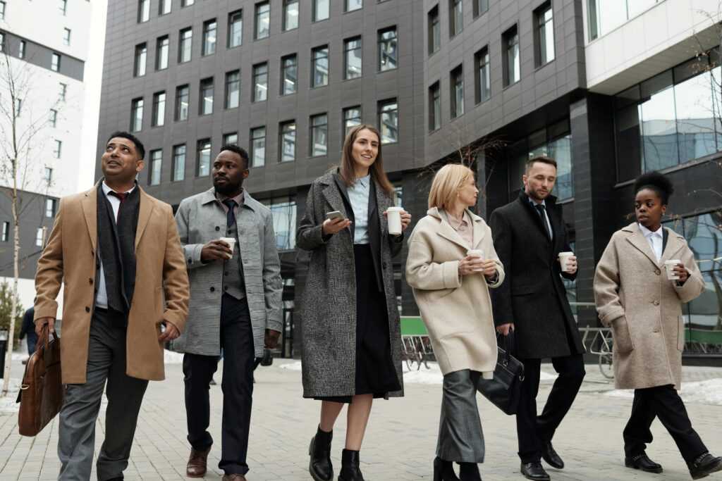 A diverse group of business professionals walking outdoors with coffee cups, showcasing teamwork.